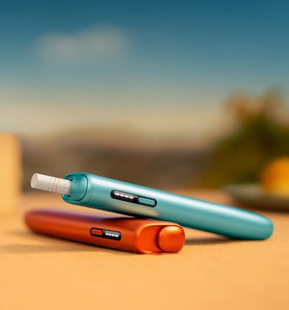 An IQOS device held by one person and a smartphone held by another person.